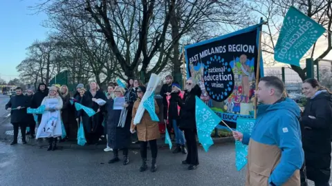 National Education Union A view of staff at Samworth Church Academy on the picket line, with NEU flags flying.
