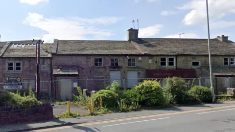 Stone two storey building with boarded up doors and windows.