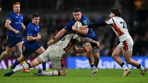 Scott Penny is tackled by Glen Young, left, and Charlie Shiel of Edinburgh during the United Rugby Championship match between Leinster and Edinburgh