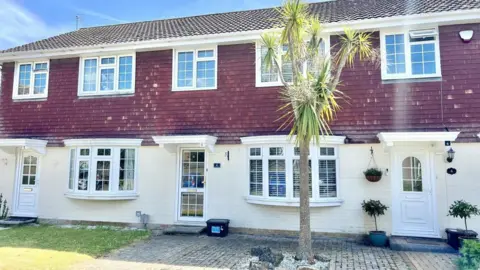 Mitchells Estate Agents A row of three terraced houses with tiled upper floors and white painted lower floor. A palm tree is in the garden.