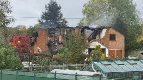 Ajay Cheema The photo shows the destroyed remains of a house with smoke coming from the roof.