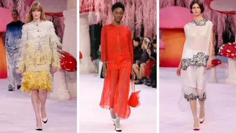 Getty Images Three models on the pink Chanel runway - one wears a tweed-style raffia suit with yellow feathers, one a red chiffon suit jacket and long skirt, and the third a sheer long-line top and skirt with black and white embellishment 