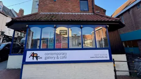 A white, blue and brick building with a sign that reads: The Art Cafe contemporary gallery & cafe.