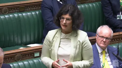 Parliament TV Layla Moran speaking in parliament on 25 Nov 2024. She has dark, curly hair and glasses and wears a light jacket and top.