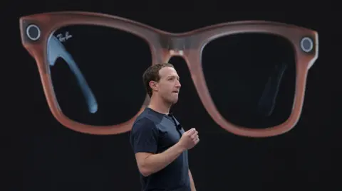 Meta CEO Mark Zuckerberg on a stage describing Meta's Ray-Bans, a large image of which is being shown behind him.