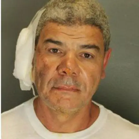 Boulder Police Department A mug shot of Mohamed Sabry Soliman who wears a white shirt, blank expression, grey hair and has a bandage on his ear and bruising on his face