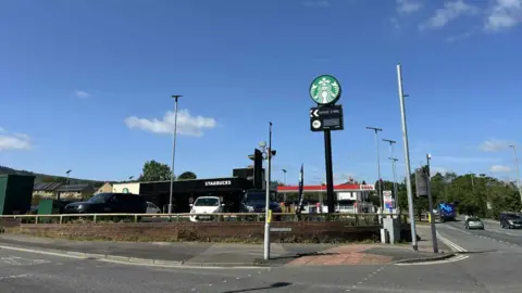 An image of a Starbucks drive-thru on the corner of a main road with a tall sign outside. 