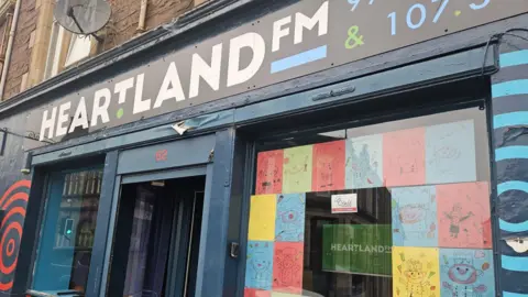 The exterior of Heartland FM's studio in Crieff. A colourful shop front with a sign saying Heartland FM above the door.