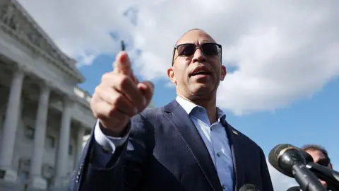 Getty Images Us House Lider mniejszości, Hakeem Jeffries, Demokrata Nowego Jorku, nosi garnitur marynarki wojennej i odcienie, gdy stoi na schodach Kapitolu USA w Waszyngtonie. Wskazuje prawy palec wskazujący, gdy przemawia do reporterów.