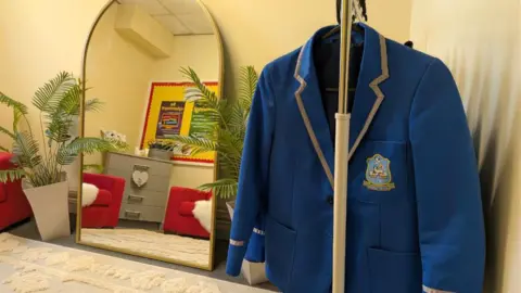 A cosy looking room with a mirror, plant, cream carpet and blue blazer hanging on a rail.