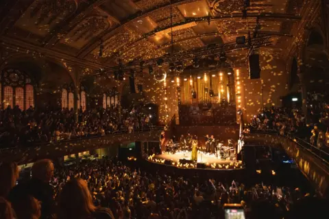 Aaron Parsons Olivia Dean is pictured on stage at Manchester's Albert Hall, which is illuminated by thousands of reflected lights from a mirrorball