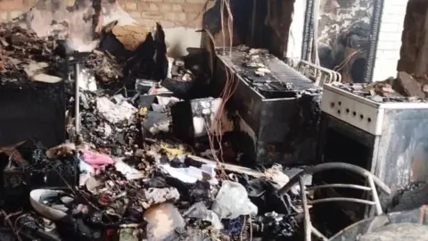 A badly fire-damaged kitchen with charred appliances and rubble.