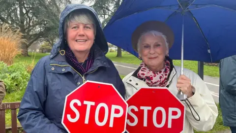 A picture of two ladies holding a sign each. It is red signs with the word STOP on it.