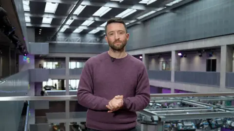 David Wallace Lockhart in BBC office in Scotland looking down the lens dressed in a purple jumper