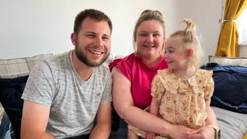 Jodie, Rich and Amelia sitting on a sofa at home smiling at the camera