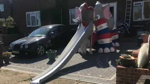 LDRS A multi-coloured elephant slide in a driveway of someone's house.