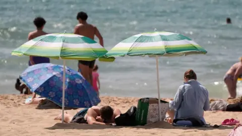 People sunbathe on a beach beneath umbrellas because of the sun.