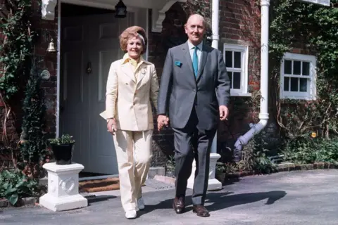 Getty Images A man and a woman both dressed in suits walking towards the camera outside the front door of a house