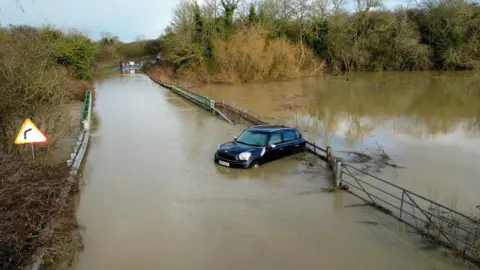 A black Mini Cooper car stuck in the middle of flooded bridge.