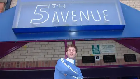 ESP Magazine Man wearing sport casual clothes in front of a sign for the 5th Avenue nightclub.