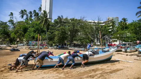 People push a boat up a sandy beach to secure it ahead of Hurricane Erick