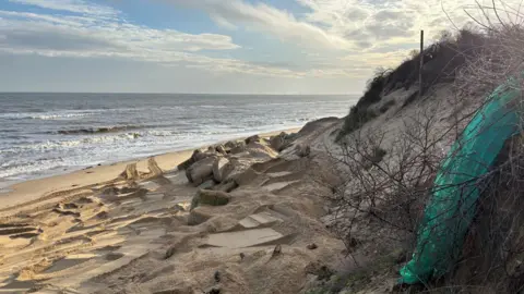 Richard Knights/BBC Erosion on Hemsby beach. Green plastic can be seeen hanging from a large sand dune