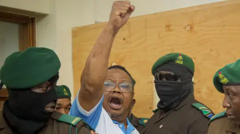 Tanzania's main opposition leader Tundu Lissu (2nd L) raises his fist in the air as he enters the court room at Kisutu magistrate's court in Dar es Salaam. He is surrounded by security officers in uniform, some with face masks