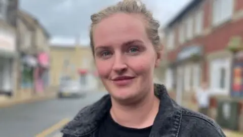 Woman with her hair pulled back and wearing a black jacket and top looks into the camera