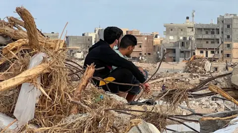 Two people sit among the wreckage after the floods.