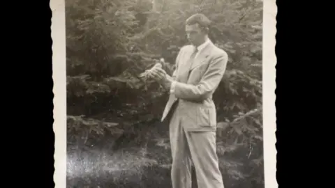 Laidlaw Auctioneers & Valuers A black-and-white photo of a man dressed in a light-coloured suit holding a pigeon.