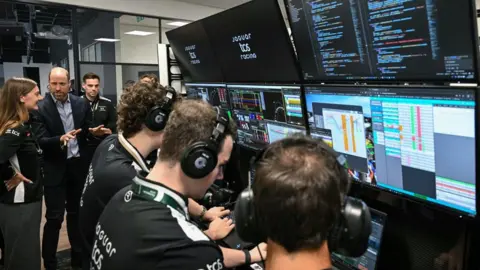 Justin Tallis/PA Wire The Prince of Wales (second left) speaks with technicians during a visit to Formula E Team Jaguar TCS Racing in Kidlington. Several of them are in front of computers, with headphones on. One is speaking with the Prince.