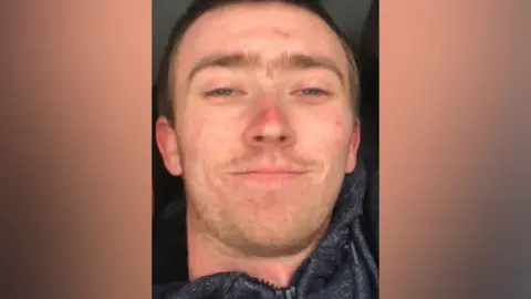 Daniel Clarke A selfie of Daniel Clarke. He has short, light brown hair and stubble, and is wearing a dark grey hoodie as he smiles at the camera
