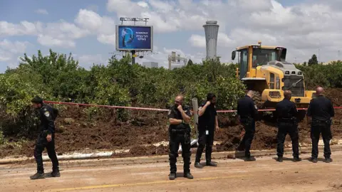 Police officers guard as a tractor works at a scene where the ballistic missile landed