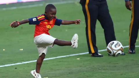 Reuters Kenye smiles as he kicks a football on the pitch