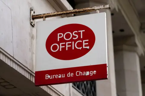 PA Media A post office sign on a building. Post Office is written in white writing on a red oval background and at the bottom of the sign is a red block with the words Bureau de Change in it