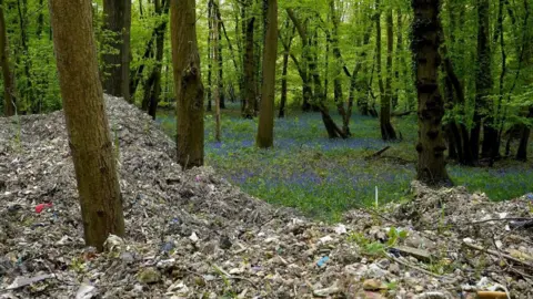 PA Media Waste piled up in the forest amid a bluebell carpet in the background