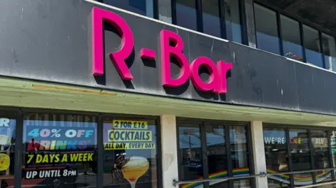 Will Flockton / BBC A black building with pink writing on the front reading "R-Bar".