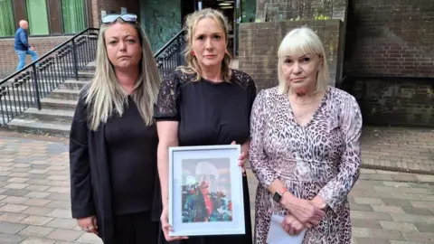 Three women stand outside Portsmouth Crown Court. The middle one holds a picture of Sammie Murphy, whose mother Denise Calver is on the right.