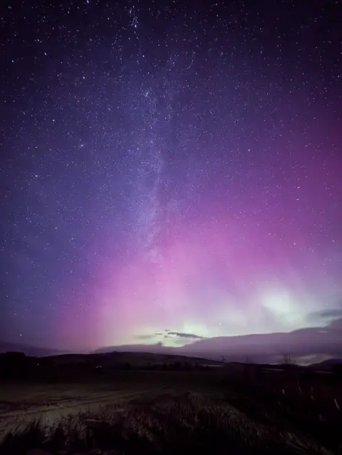 Pete Walls A blue and purple starry night thanks to the Aurora, over a hillside.