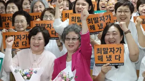 News1 Choi Mal-ja (in pink) surrounded by her lawyers and supporters, as they smile and pump their fists into the air in victory