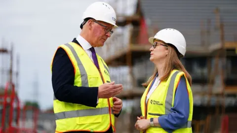 PA Media A man and woman face each other while wearing high-visibility vests and hard hats 