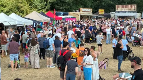 Large crowds of people gathered at the open day event. There are numerous stalls in the background. 