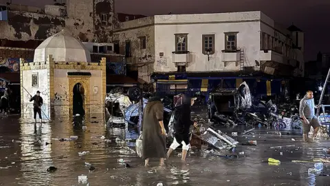 AFP via Getty Images People wade through floodwaters in the old city centre.