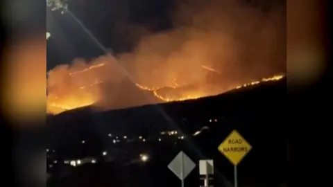 Picture taken at night showing fires burning on hill, plumes of white smoke covering the skies