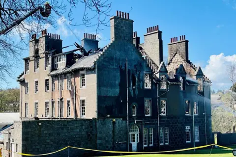 Firefighters in a height vehicle using water to dampen down the shell of a building hit by fire.
