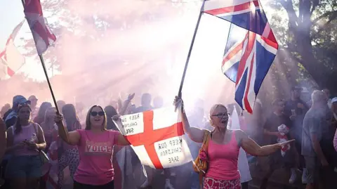 A protest outside the Bell Hotel. Two women are holding St George and Union flags. On one flag is written the message: "Keep our children safe". 