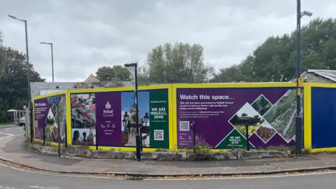 A section of Moat Street is behind purple boards. They have image of houses, greenery and Walsall Council insignia on.