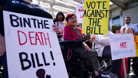 PA Media Demonstrators, some in wheelchairs, with placards showing their opposition to the bill