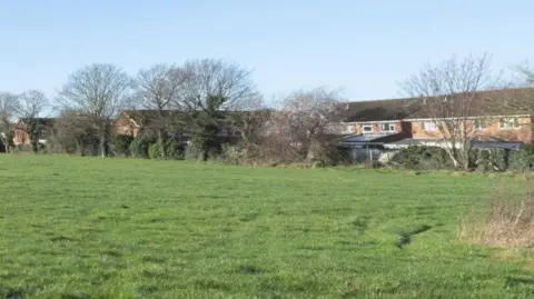 Aster Homes Ltd/CBC The Folly field, with a row of trees in front of local houses