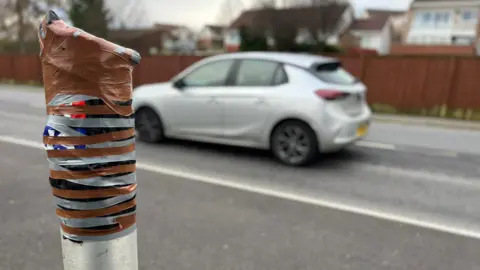 This is the stretch of the A4102 in Merthyr Tydfil which has seen 8,000 offences, although the camera was out of action when we visited. It appears the camera - in  layby -  has been broken off and the post has been taped up. Photo shows a black VW car driving past.